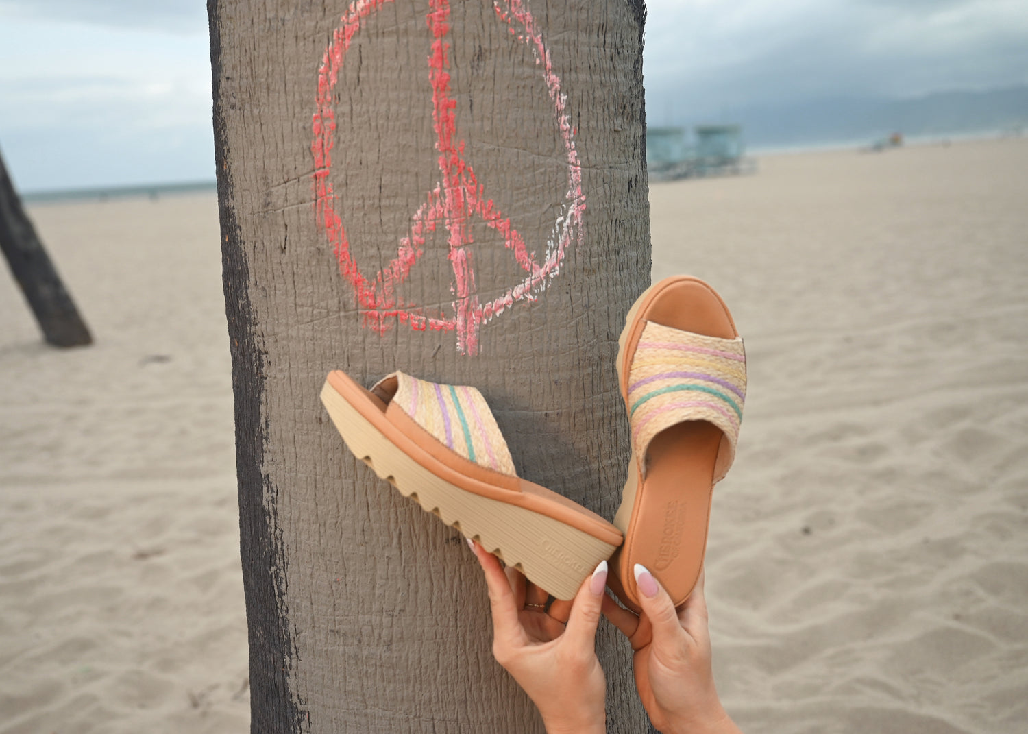 Pair of sandals on a beach with a peace symbol in the background